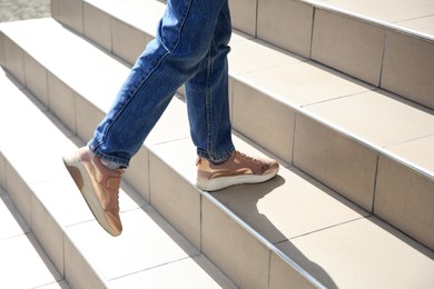 Photo of Woman walking up beige stairs on sunny day, closeup