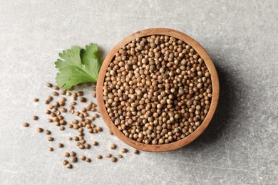 Photo of Dried coriander seeds in bowl and green leaf on light gray textured table, flat lay
