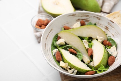 Photo of Delicious pear salad in bowl on light tiled table, closeup. Space for text