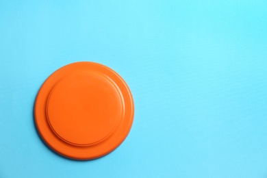 Photo of Orange plastic frisbee disk on light blue background, top view. Space for text