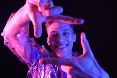 Photo of Young man making camera with hands on dark background in neon lights
