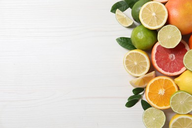 Photo of Different cut and whole citrus fruits on white wooden table, top view. Space for text