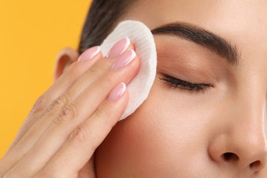 Photo of Beautiful woman removing makeup with cotton pad on orange background, closeup
