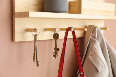 Photo of Wooden rack with hanging keys, jacket and purse on beige wall indoors