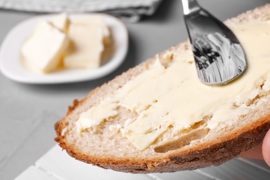 Photo of Spreading tasty butter on slice of fresh bread, closeup