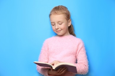 Photo of Happy little girl reading book on light blue background