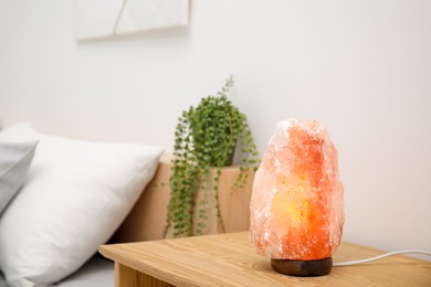 Photo of Himalayan salt lamp on wooden table in bedroom, space for text