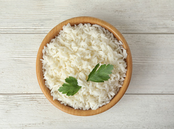 Photo of Bowl with tasty cooked rice and parsley on white wooden table, top view