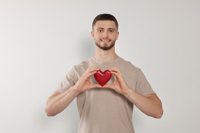 Photo of Happy volunteer holding red heart with hands on light background