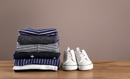 Photo of Stack of baby boy's clothes and shoes on wooden table against brown background, space for text