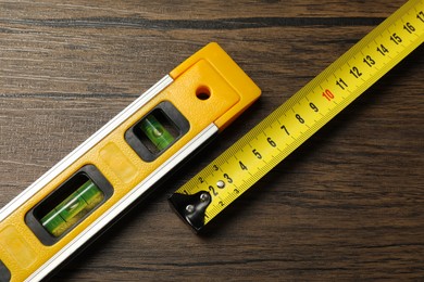 Photo of Building level and tape measure on wooden table, top view