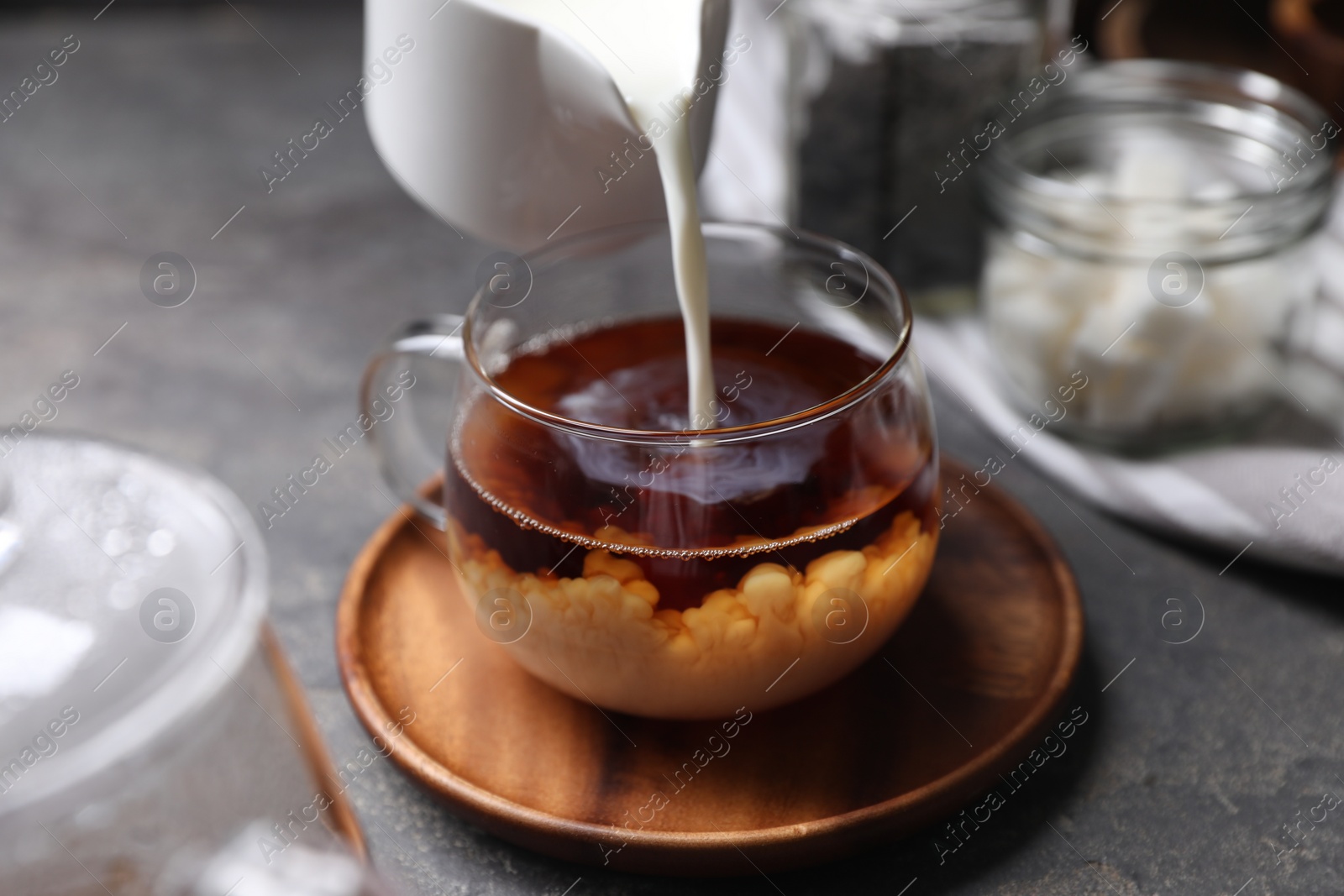 Photo of Pouring milk into cup of tea on grey table, closeup