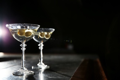 Photo of Glasses of martini cocktail with olives on bar counter. Space for text