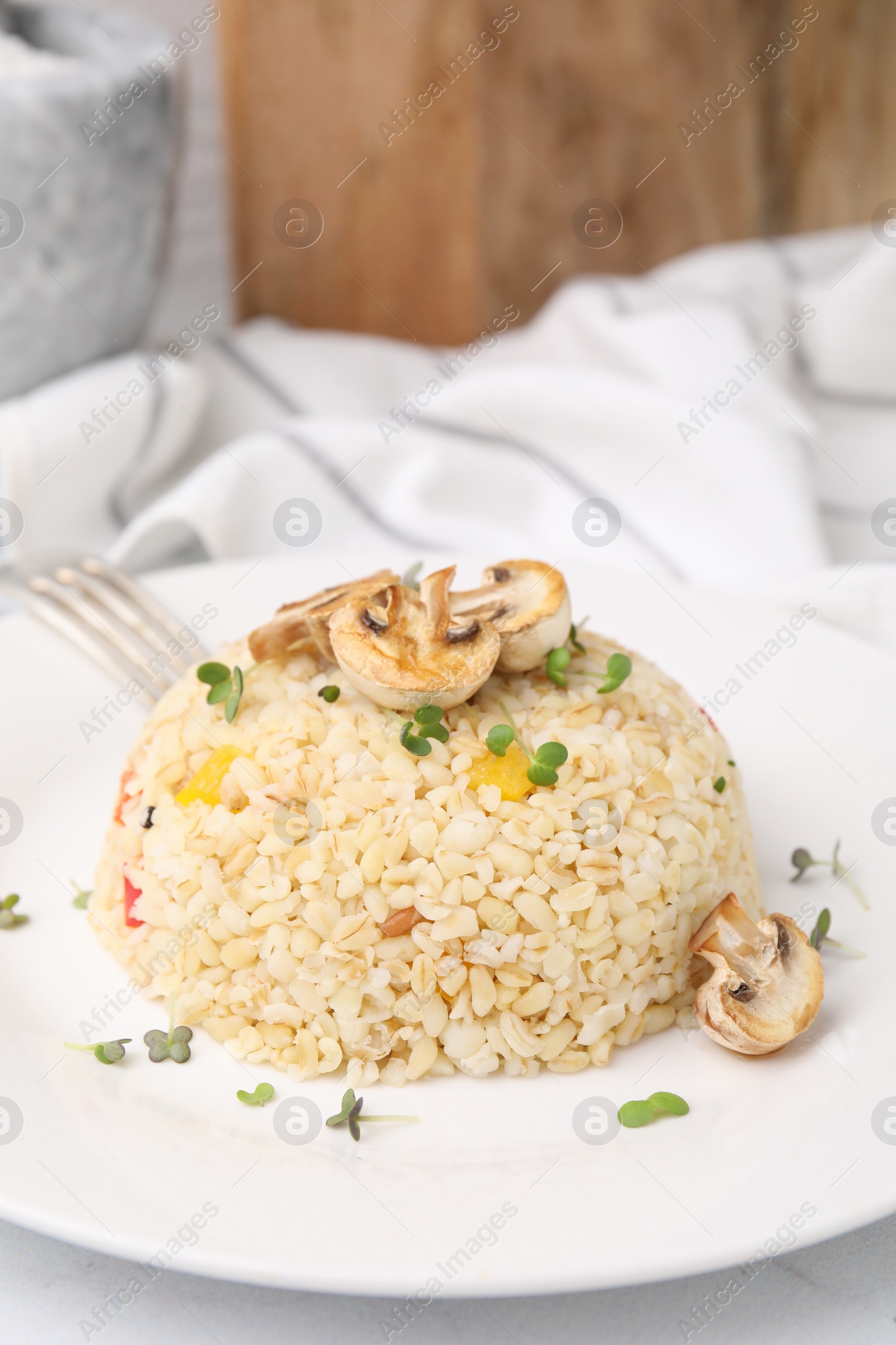 Photo of Delicious bulgur with vegetables, mushrooms and microgreens on table, closeup