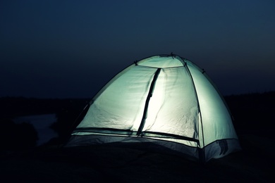 Photo of Small camping tent glowing in twilight outdoors. Space for text