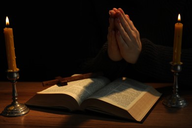 Photo of Woman praying at table with burning candles and Bible, closeup