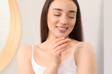 Photo of Woman applying essential oil onto shoulder in bathroom, closeup