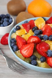 Photo of Delicious fresh fruit salad in bowl served on wooden table, closeup