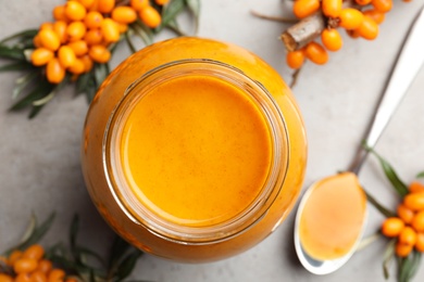 Photo of Delicious sea buckthorn jam and fresh berries on grey table, flat lay