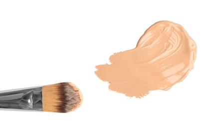 Photo of Sample of liquid foundation and makeup brush on white background, top view