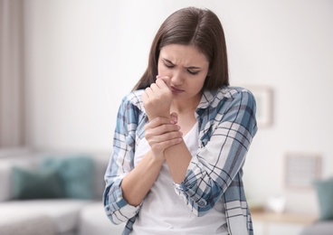 Photo of Young woman suffering from hand pain at home