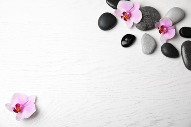 Photo of Stones with orchid flowers and space for text on white wooden background, flat lay. Zen lifestyle