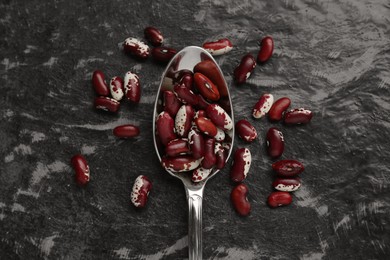 Photo of Metal spoon and dry kidney beans on black textured table, flat lay