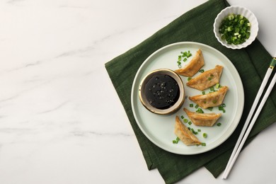 Photo of Delicious gyoza (asian dumplings) with soy sauce, green onions and chopsticks on white marble table, top view. Space for text