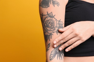 Photo of Woman with tattoos on arm against yellow background, closeup. Space for text