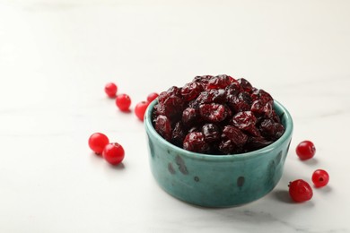 Photo of Tasty dried cranberries in bowl and fresh ones on white marble table, closeup. Space for text