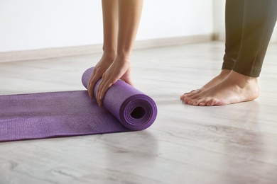 Photo of Woman rolling yoga mat on floor indoors, closeup