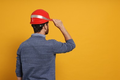 Photo of Professional engineer in hard hat on yellow background, back view. Space for text