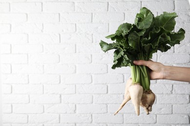 Photo of Woman holding sugar beets against white brick wall, closeup. Space for text