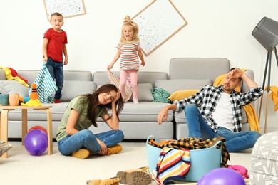 Photo of Frustrated parents and their mischievous children in messy room