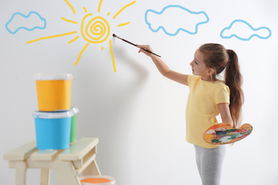 Image of Cute child drawing sky with sun on white wall indoors