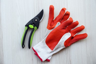 Photo of Secateurs and gardening gloves on white wooden table, flat lay