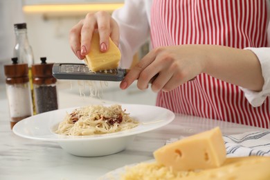 Photo of Woman grating cheese onto delicious pasta at white marble table in kitchen, closeup