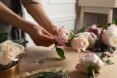 Photo of Florist creating beautiful bouquet at wooden table indoors, closeup