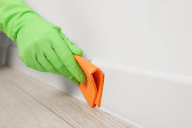 Photo of Woman in protective glove cleaning plinth with sponge cloth indoors, closeup. Space for text