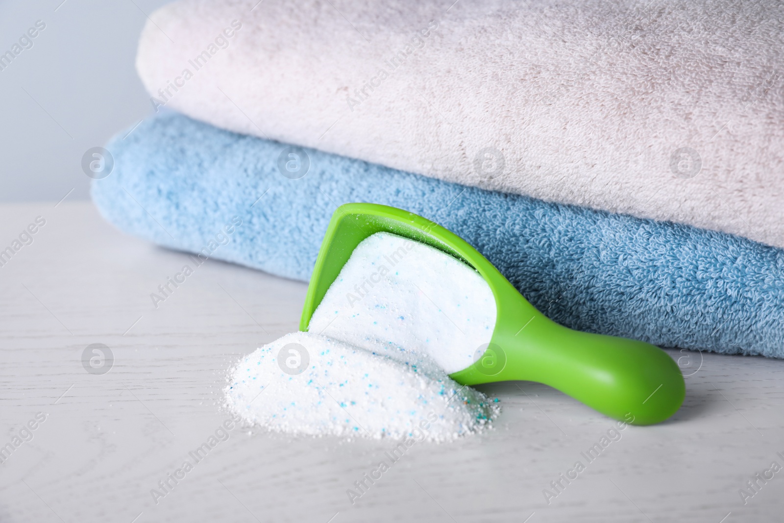 Photo of Measuring scoop and scattered laundry powder near towels on table