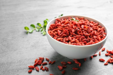 Photo of Bowl of dried goji berries on grey table, space for text. Healthy superfood