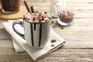 Photo of Delicious hot chocolate with marshmallows and cocoa powder in cup on wooden table, space for text