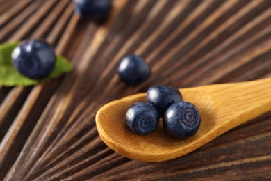 Spoon with tasty fresh bilberries on wooden table, closeup