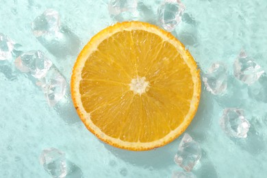 Photo of Slice of juicy orange and ice cubes on light blue background, top view