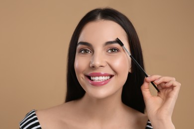 Photo of Happy woman applying makeup with eyebrow brush on light brown background
