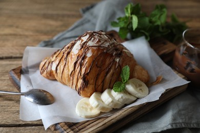 Photo of Delicious croissant with chocolate, banana and spoon on wooden table