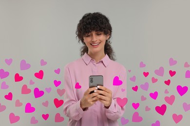 Image of Long distance love. Woman chatting with sweetheart via smartphone on grey background. Hearts around her