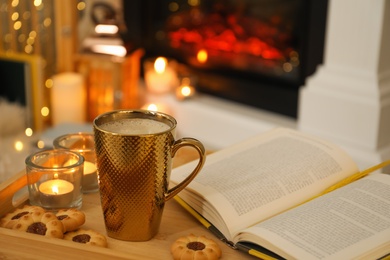 Photo of Cup of coffee, book and cookies on wooden tray indoors