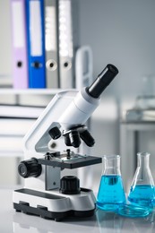 Photo of Different laboratory glassware with light blue liquid and microscope on table