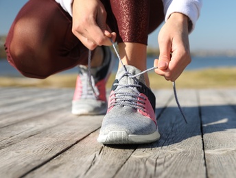 Image of Sporty woman tying shoelaces outdoors on sunny morning, closeup